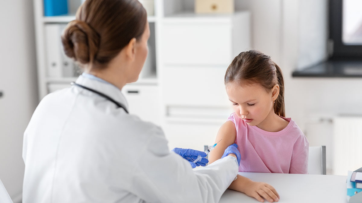 medicine, healthcare and vaccination concept - female doctor or pediatrician with syringe making vaccine injection to little girl patient at clinic