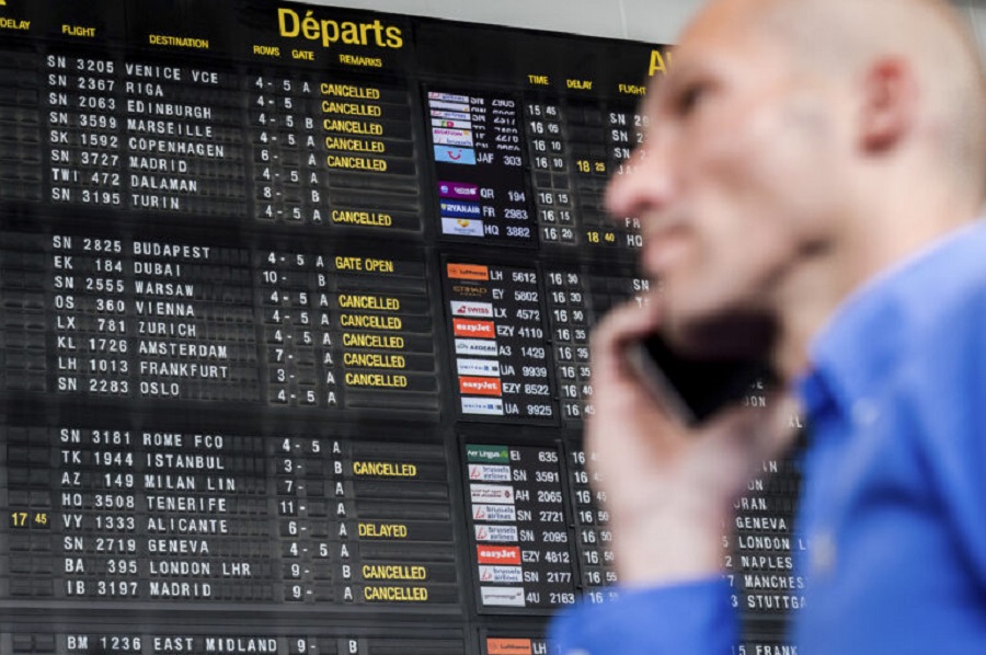 FILE - In this Wednesday, May 27, 2015, file photo, a passenger makes a phone call as he walks by a flight information board at Brussels Airport in Zaventem, Belgium. You don’t have to pay a fortune to use your phone abroad, but you need to plan ahead. Getting a local plan when you arrive is the most economical choice, but it’s not practical for many people. (AP Photo/Geert Vanden Wijngaert, File)