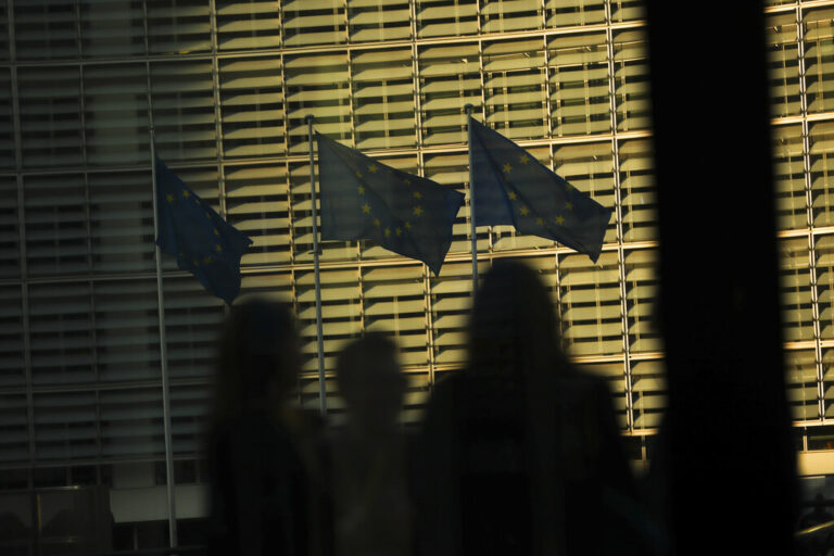 Members of the media look toward EU flags flapping in the wind outside EU headquarters during an EU summit in Brussels, Thursday, March 21, 2019. British Prime Minister Theresa May is trying to persuade European Union leaders to delay Brexit by up to three months, just eight days before Britain is scheduled to leave the bloc. (AP Photo/Francisco Seco)