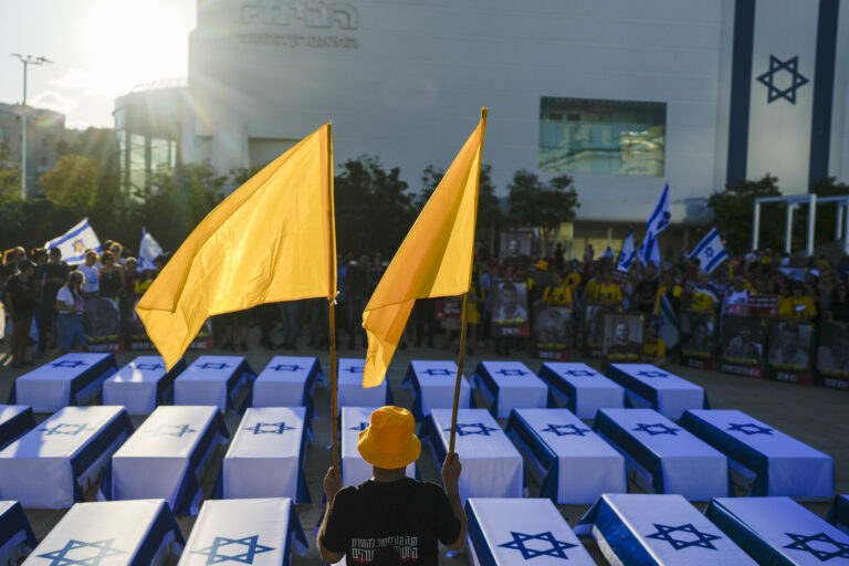 A man holds flags next to mock coffins covered Israeli flags representing the 27 hostages whose bodies have been recovered from Gaza, during a rally demanding a cease-fire deal and the immediate release of hostages held by Hamas in the Gaza Strip on Thursday, Sept. 5, 2024, in Tel Aviv, Israel. (AP Photo/Ohad Zwigenberg)