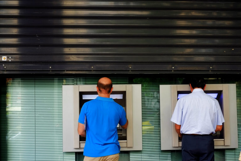 Men use the ATM outside of a closed bank five days before the upcoming referendum, in central Athens, on Tuesday, June 30, 2015. Greek Finance Minister Yanis Varoufakis confirmed that the country will not make its payment due later to the International Monetary Fund. Capital controls began Monday and will last at least a week, an attempt to keep the banks from collapsing in the face of a nationwide bank run. (AP Photo/Petros Karadjias)