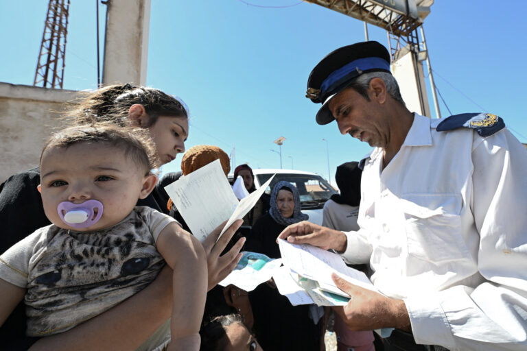 A border policeman checks the documents of a woman carrying a baby, after she entered Syria from Lebanon via the Jusiyeh border crossing with Quseir in Syria's central Homs province on October 2, 2024. Lebanon said on October 2 that almost 240,000 people, mostly Syrians, have crossed to Syria since Israel began pounding the country last week with intense air strikes on what it says are Hezbollah targets. (Photo by LOUAI BESHARA / AFP)