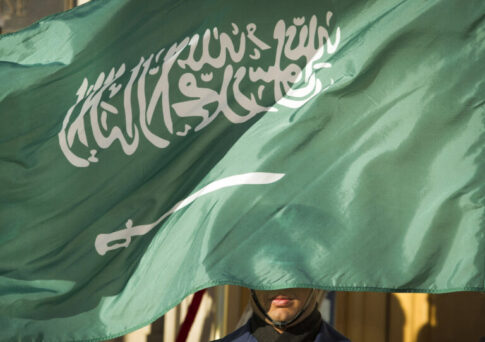 FILE - In this March 22, 2018, file photo, an honor guard member is covered by the flag of Saudi Arabia, in Washington. Three young Saudi men who faced death sentences for acts they were accused of committing as minors have been handed a 10-year prison sentence instead, the Saudi Human Rights Commission said. The move comes nearly a year after Saudi Arabia ordered an end to the death penalty for crimes committed by minors. Crown Prince Mohammed bin Salman, is the force behind the kingdom’s efforts to modernize the country and loosen restrictions. (AP Photo/Cliff Owen, File)