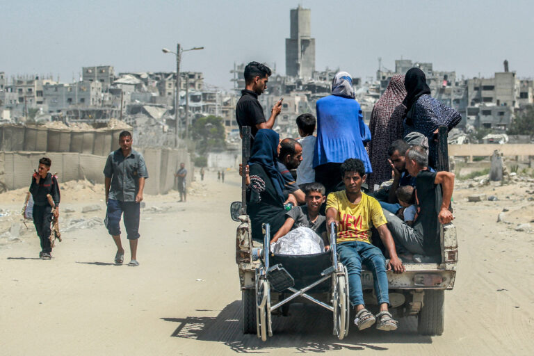 People sit in the back of a truck moving along a road in Khan Yunis in the southern Gaza Strip on June 18, 2024 amid the ongoing conflict in the Palestinian territory between Israel and Hamas. (Photo by Bashar TALEB / AFP)