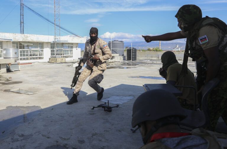 A Haitian police officer runs to take cover with Kenyan police officers, part of a UN-backed multinational force, during an exchange of gunfire with gangs at a Kenyan police base in the Delmas neighborhood of Port-au-Prince, Haiti, Thursday, Dec. 5, 2024. (AP Photo/Odelyn Joseph)