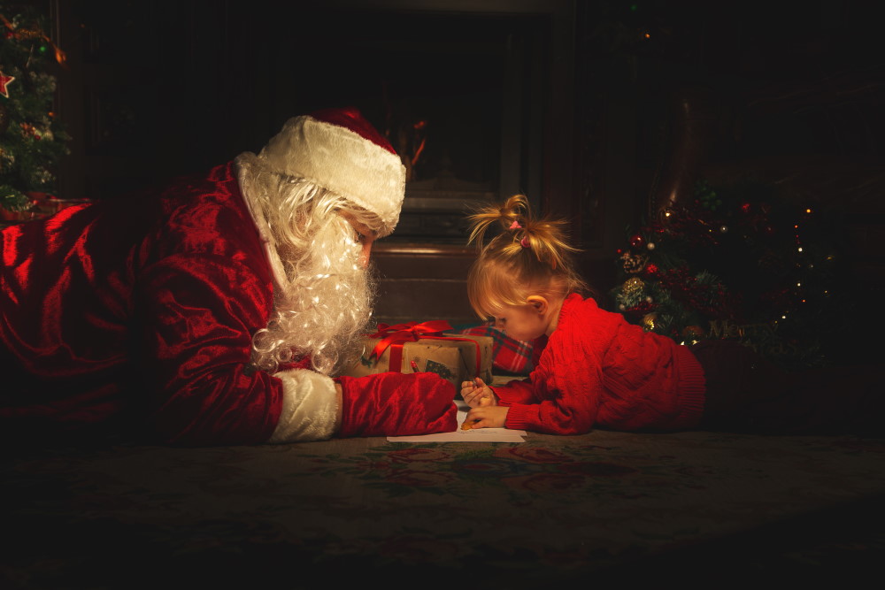 Real Santa Claus is playing with children near the Christmas tree. The atmosphere of celebration and magic.