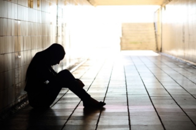 Backlight of a teenager depressed sitting inside a dirty tunnel