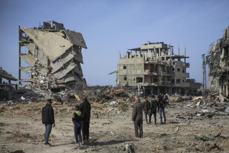 FILE - Palestinians stand near buildings destroyed by an Israeli air and ground offensive, Jan. 19, 2025, in Rafah. (AP Photo/Mohammad Hajjar, File)